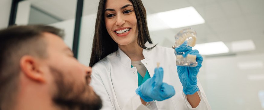 Dentist showing dental implant to patient in modern clinic